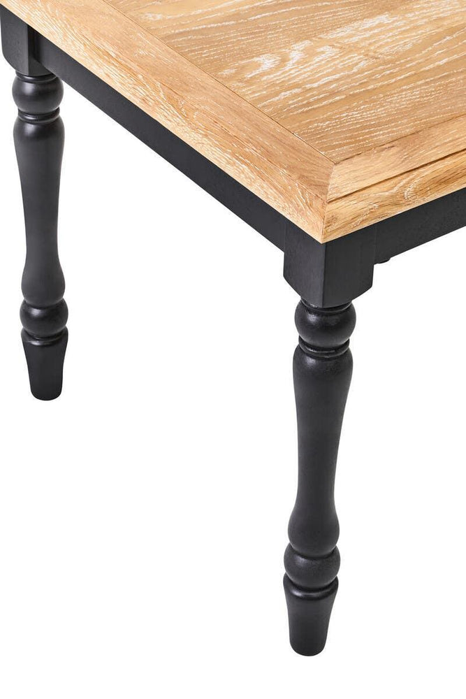 Oak wood dining table corner with turned black legs and light grain tabletop finish