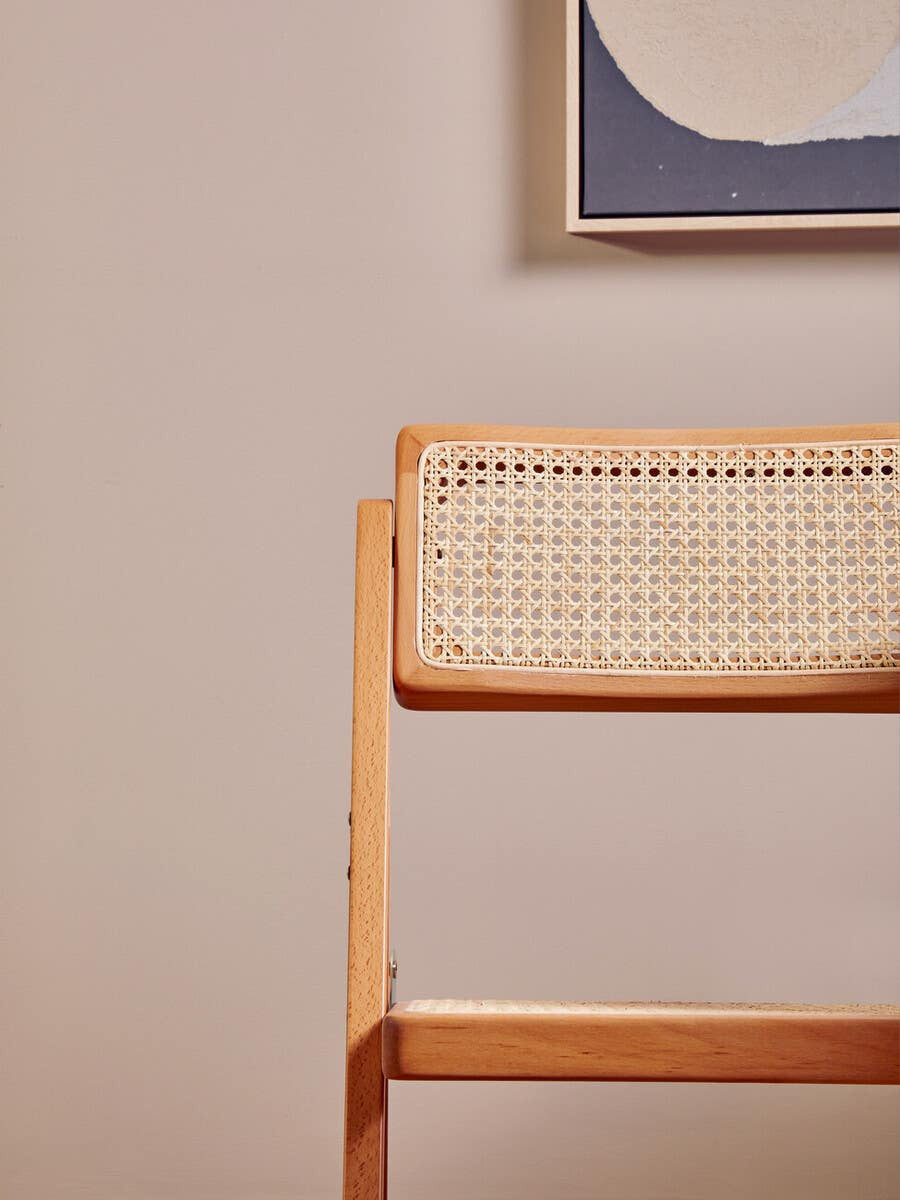 Cebu Beech Wood Frame Folding Chair featuring a light wooden frame with a woven seat and backrest, set against a neutral wall with abstract artwork in the background