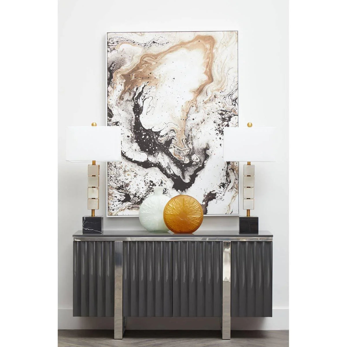 Grey sideboard with metallic legs, two table lamps, glass vases, and abstract wall art
