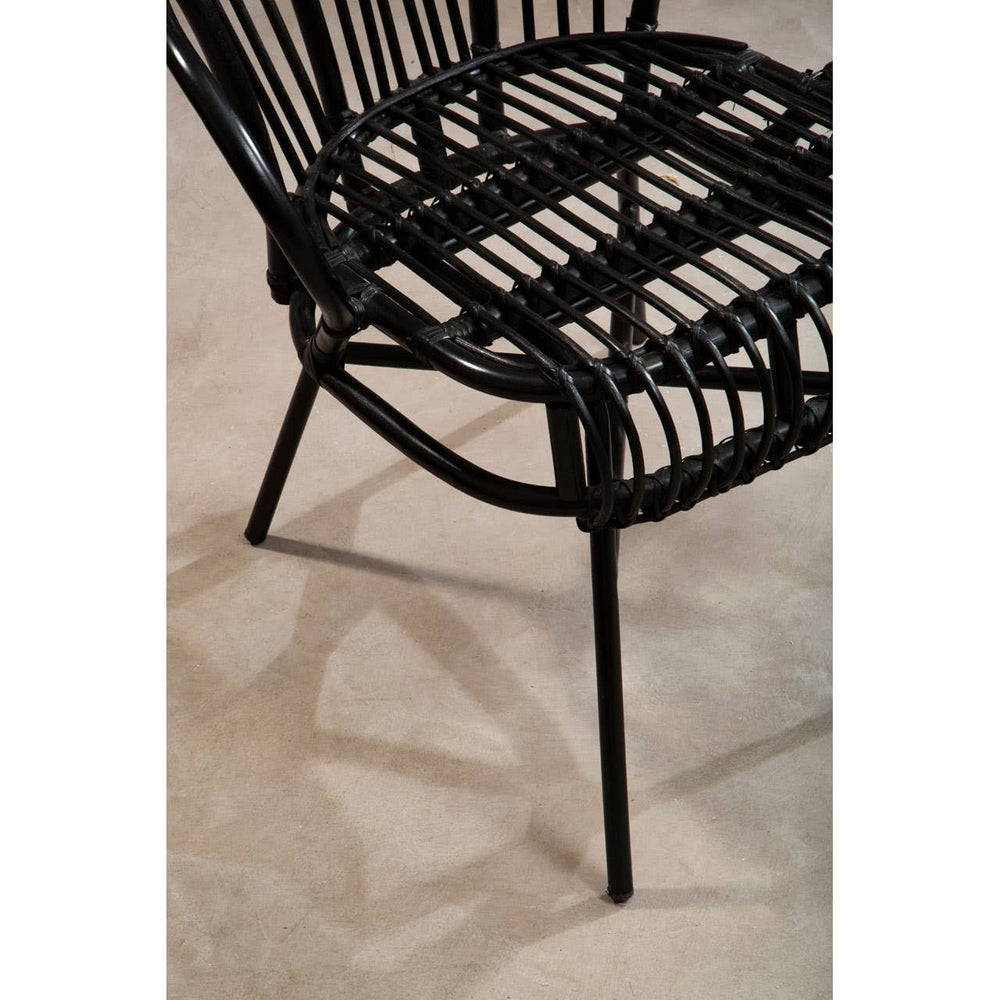 A black metal chair with a scalloped back design, featuring natural rattan weaving on the seat and backrest. The chair has slender legs and is positioned on a light-colored floor, casting a subtle shadow