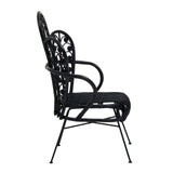 A side view of a black rattan chair featuring a scalloped back design, slender armrests, and a cushioned seat, supported by thin metal legs