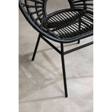 A black rattan flared back chair with a circular seat and open weave design, supported by slender black metal legs, placed on a light-colored floor