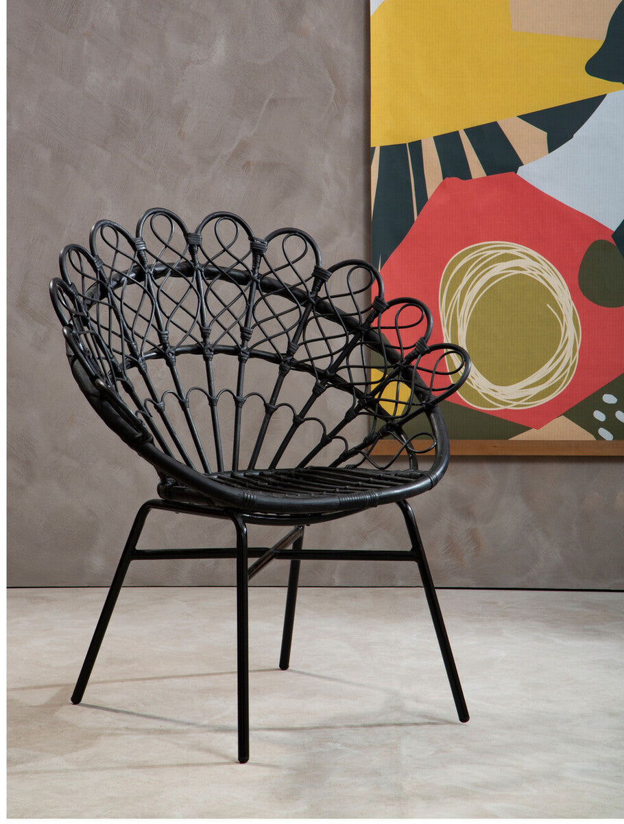 A stylish black rattan peacock chair with a distinctive fan-shaped backrest, set against a textured gray wall and colorful abstract artwork in the background. The chair features slender legs and a modern design, perfect for adding a touch of elegance to any space