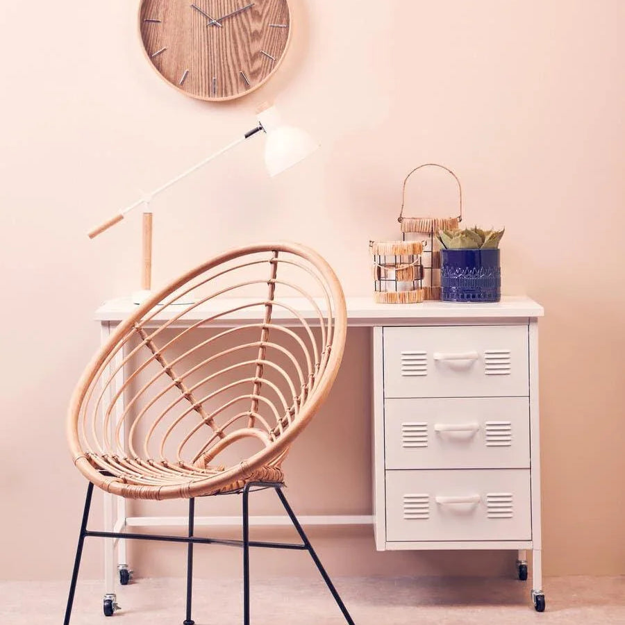 Rattan accent chair with black metal legs beside white desk and wooden wall clock
