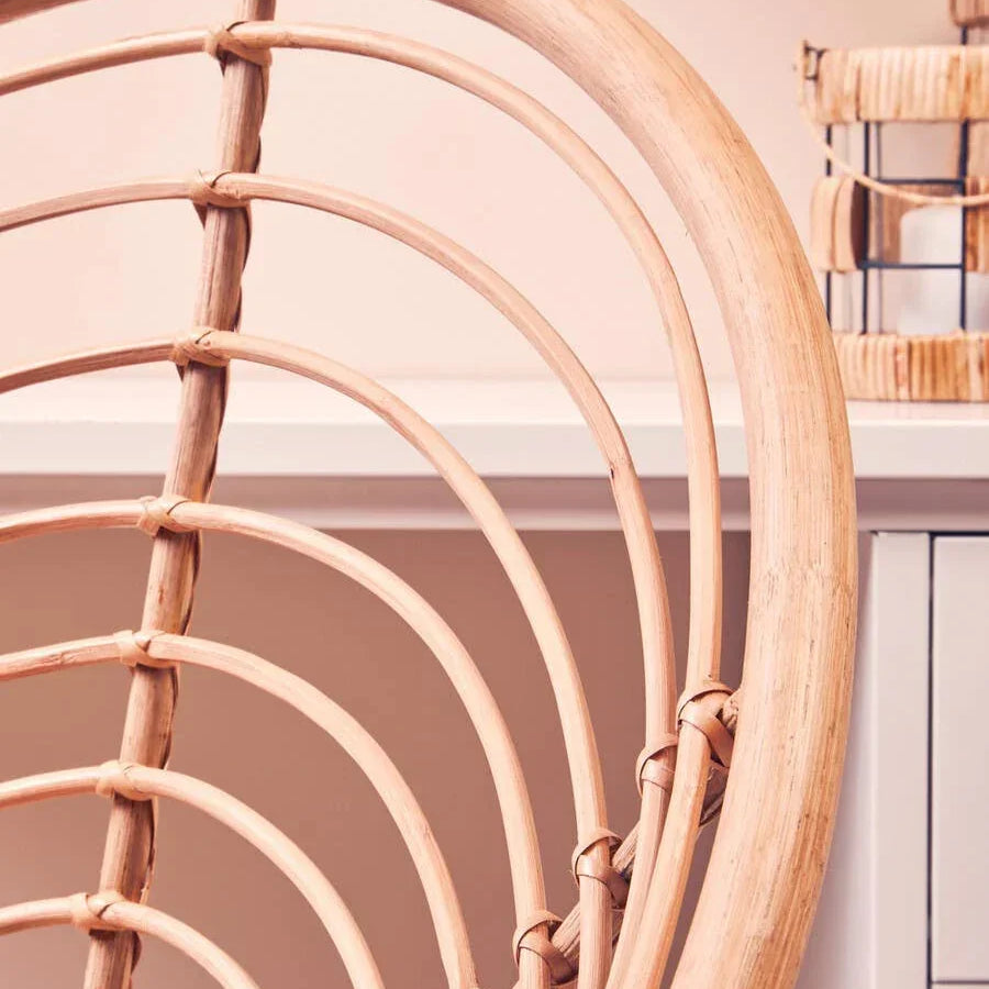 Curved rattan chair backrest in natural finish near white cabinet and decorative lantern