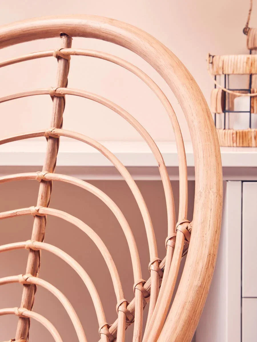 Curved rattan chair backrest in natural finish near white cabinet and decorative lantern
