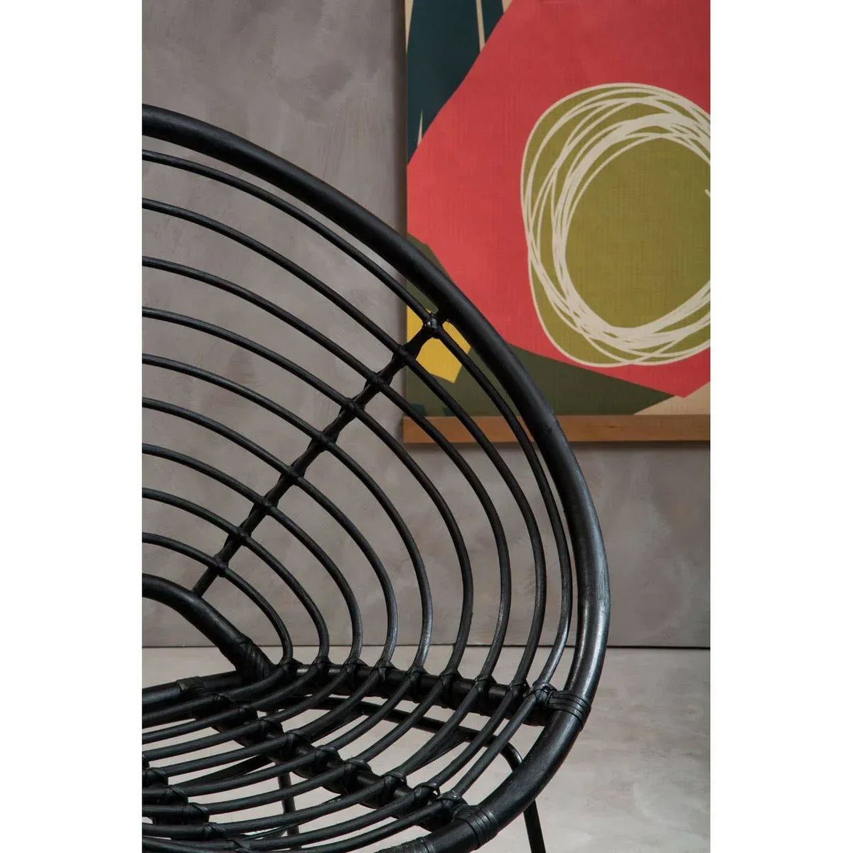 Black rattan chair curved seat detail with modern abstract wall art in background
