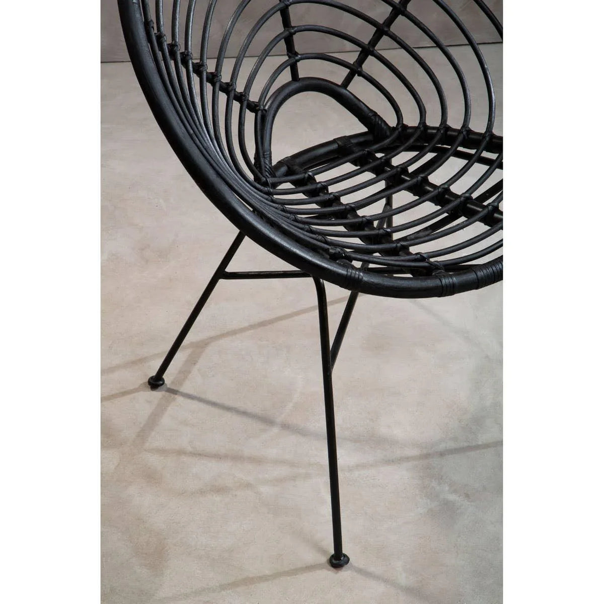 Black rattan accent chair with round seat and metal legs on light flooring