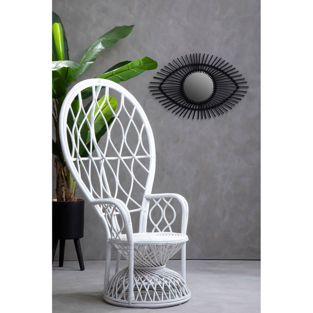 Curved chair made of natural rattan in grey and white, featuring a tall backrest with a woven pattern. The chair is positioned against a textured grey wall, with a decorative round mirror above it and a green plant in the background