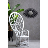Curved chair made of natural rattan in grey and white, featuring a tall backrest with a woven pattern. The chair is positioned against a textured grey wall, with a decorative round mirror above it and a green plant in the background