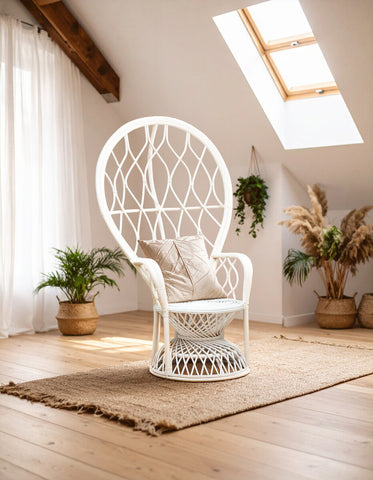 Curved chair made of natural rattan in grey and white, featuring a high back and a comfortable seat cushion, positioned on a wooden floor with a light-colored rug. Soft natural light filters through a skylight, illuminating the chair and surrounding potted plants