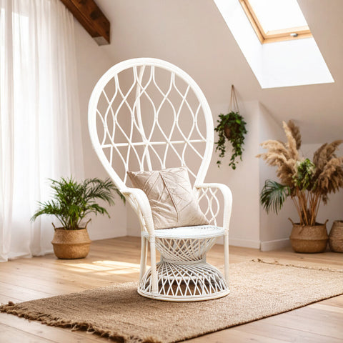 Curved chair made of natural rattan in a grey and white color scheme, featuring a large, open back design and a plush cushion. The chair is positioned on a textured rug in a bright, airy room with wooden beams and potted plants in the background. Sunlight streams through a skylight, enhancing the cozy atmosphere