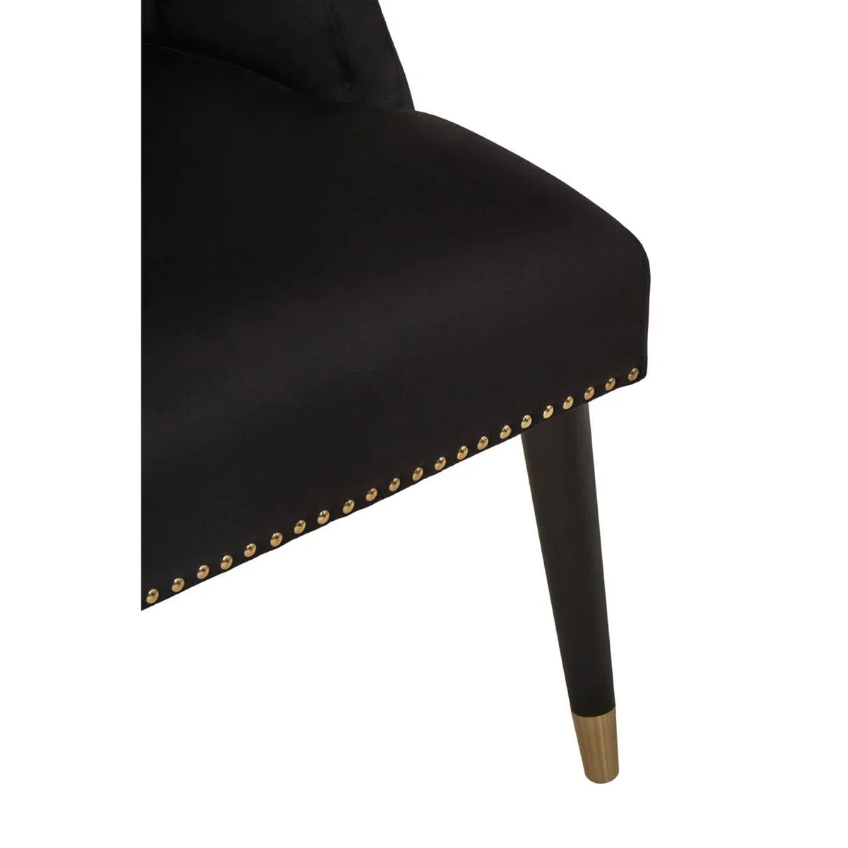 Black velvet dining chair close-up with gold stud trim and tapered leg with gold tip
