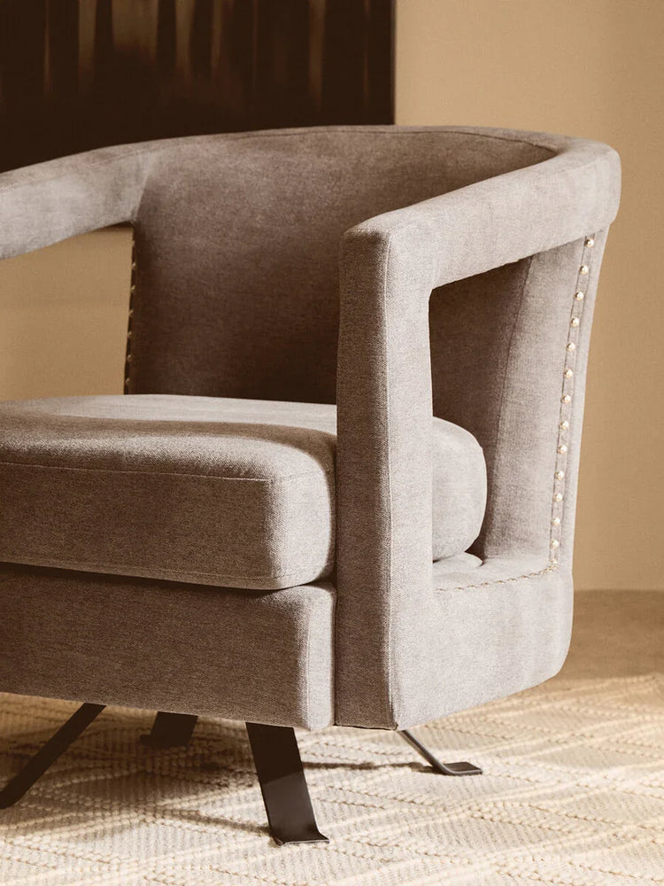 Modern grey fabric accent chair with metal legs and stud detailing on carpet