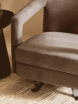 Close-up of brown fabric armchair with nailhead trim beside black side table on patterned rug