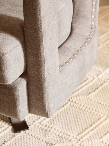 Closeup of grey fabric sofa arm with silver stud detail on textured cream rug