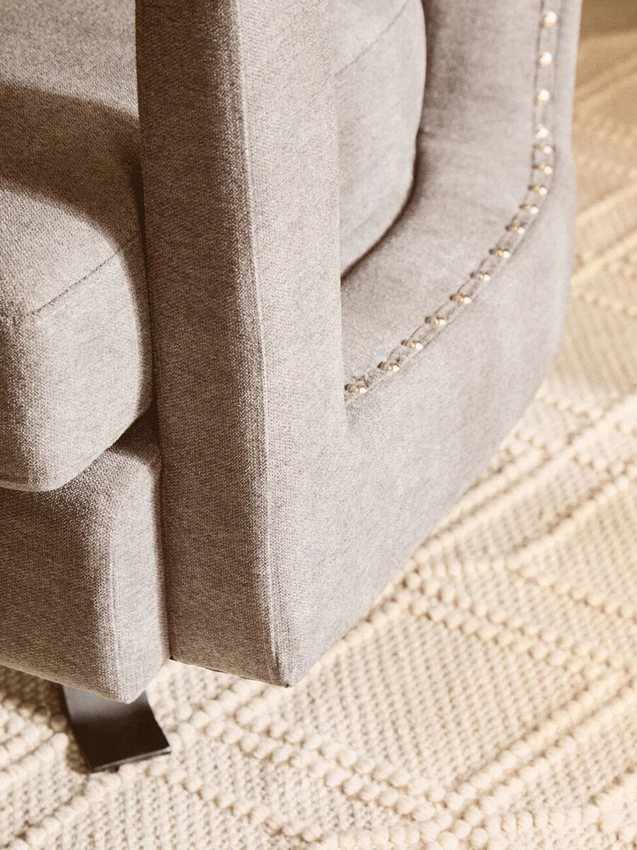 Closeup of grey fabric sofa arm with silver stud detail on textured cream rug