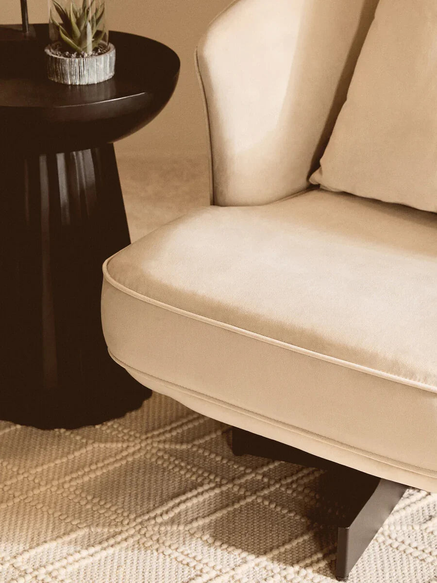 Beige upholstered armchair with cushion beside black side table on textured rug