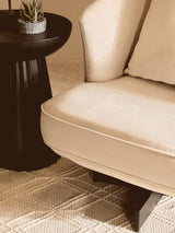 Beige upholstered armchair with cushion beside black side table on textured rug