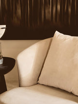 Beige velvet sofa corner with cushion beside a dark modern side table