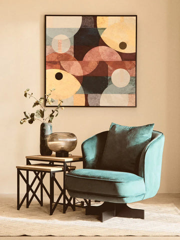 Teal velvet accent chair with cushion beside nested side tables and abstract wall art