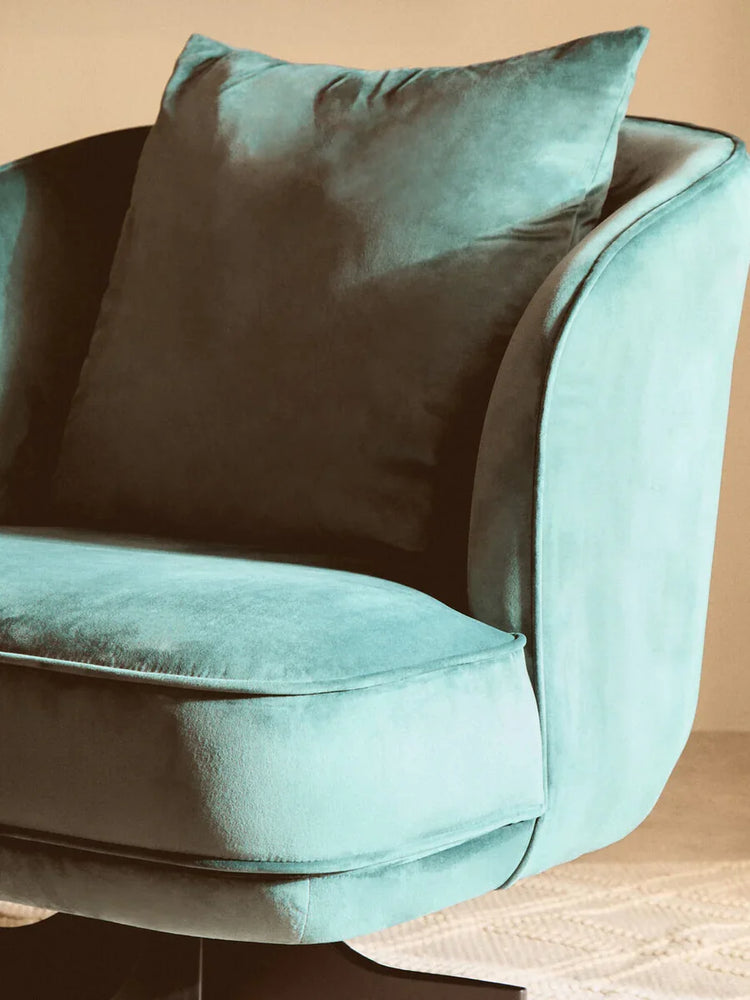 Teal velvet armchair with plush cushion and curved backrest on beige carpet
