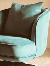 Teal velvet armchair with plush cushion and curved backrest on beige carpet