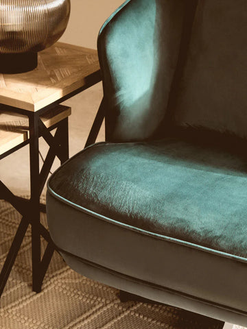 Teal velvet armchair with rounded seat beside wooden side table and ribbed lamp base