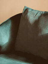 Green velvet sofa with plush back cushion against beige wall