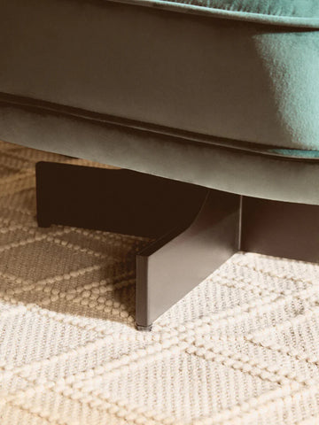 Close-up of velvet sofa base with black metal leg on textured cream rug