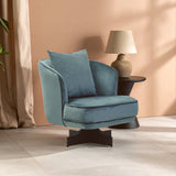 Blue velvet swivel armchair with cushion beside round black side table and beige lamp