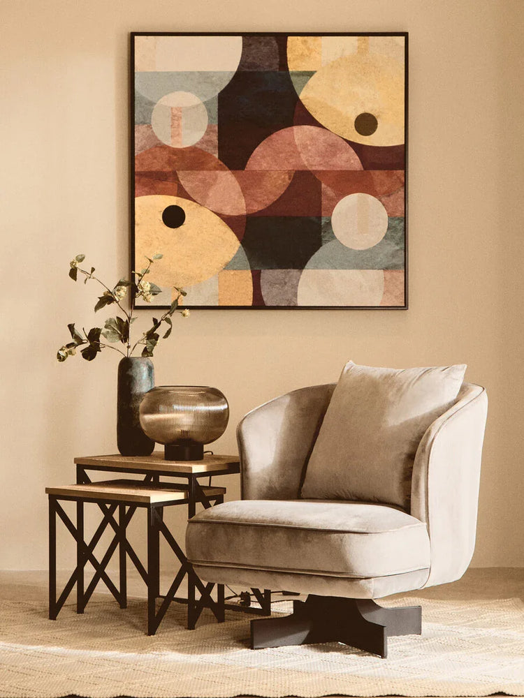 Beige velvet accent chair with black metal base beside nesting tables and abstract wall art