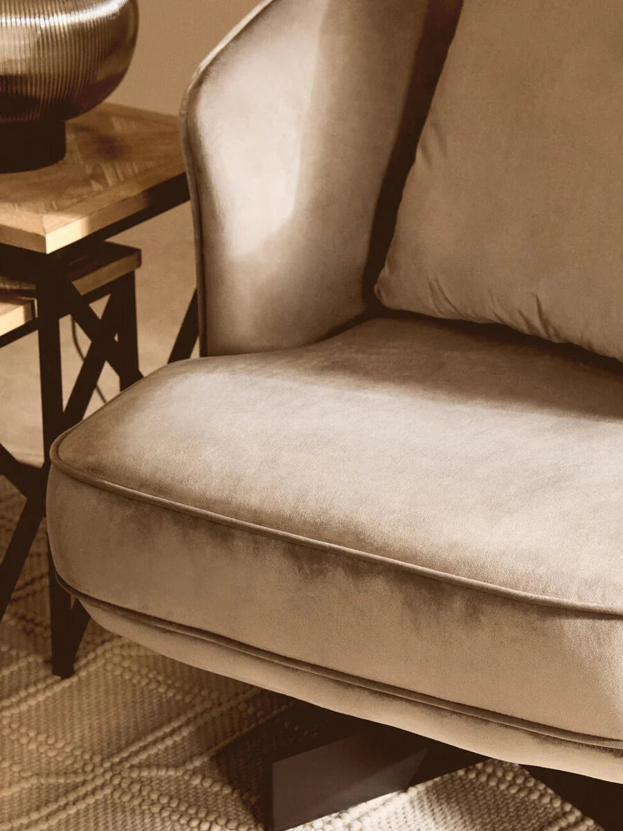 Close-up of beige velvet sofa cushion beside wooden side table on textured rug