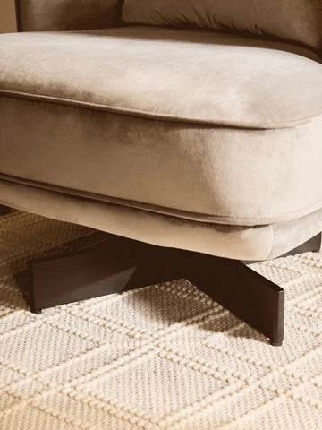 Beige velvet sofa with black metal legs on textured cream rug