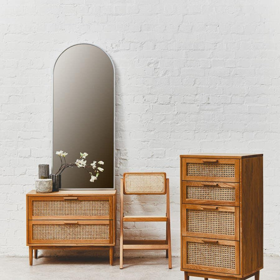 Rattan and wood chest of drawers, dresser, and chair set with an arched mirror on white brick