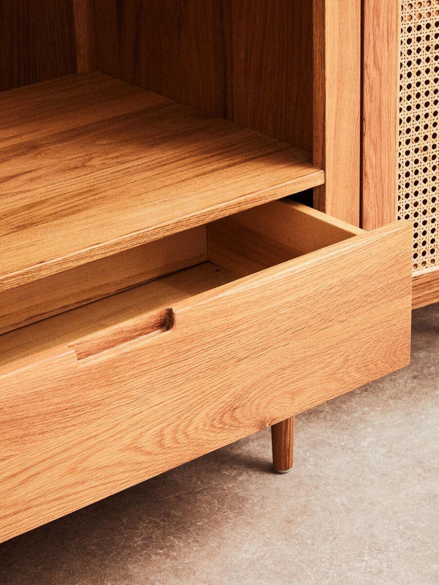 Close-up view of the Lyon Rattan and Oak Wood 2 Door Wardrobe, showcasing a wooden drawer partially open, revealing a smooth interior. The wardrobe features a natural oak finish with a sleek design, highlighting the texture of the wood and the rattan accents on the doors. The background is a soft, neutral carpet