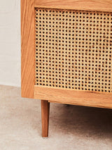 Close-up view of the lower section of the Lyon Rattan and Oak Wood 2 Door Wardrobe, showcasing the natural rattan weave on the doors and the smooth oak wood frame. The wardrobe stands on four tapered wooden legs, highlighting its modern design and craftsmanship. The background features a neutral-toned surface, enhancing the warm tones of the wood