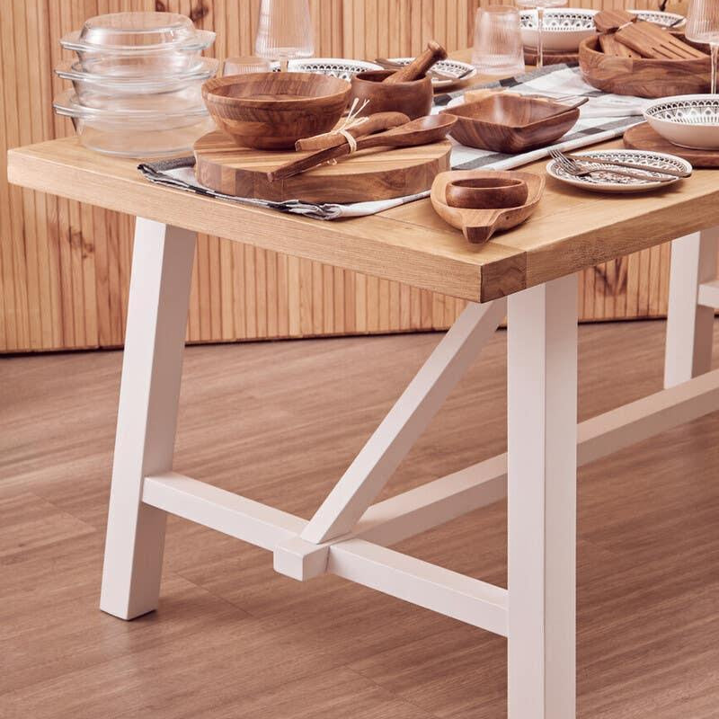 Wooden dining table with white legs set with bowls, plates, utensils and glassware