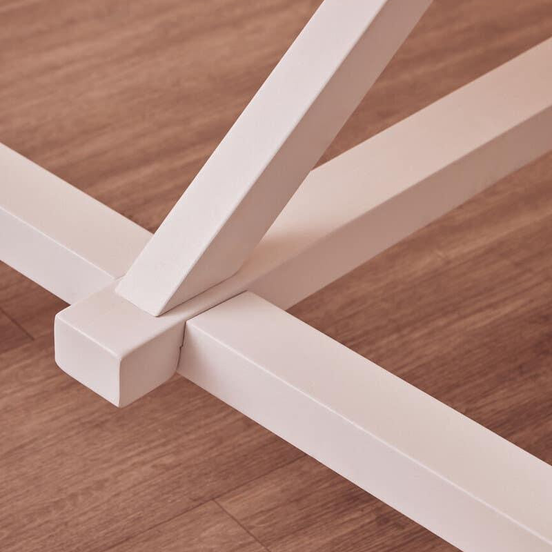 Closeup of white metal table legs with cross base on wood floor