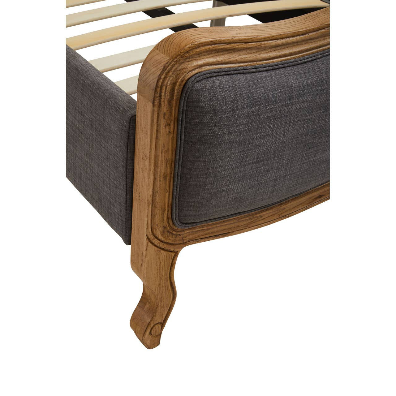 The corner of a super kingsize bed featuring a grey fabric upholstery and a wooden frame with a curved design. The wooden leg is elegantly shaped, showcasing a classic style. The slatted base is visible inside the bed frame