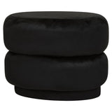A plush black velvet oval pouffe with a smooth surface and a rounded, stacked design, suitable for use as a footrest or additional seating