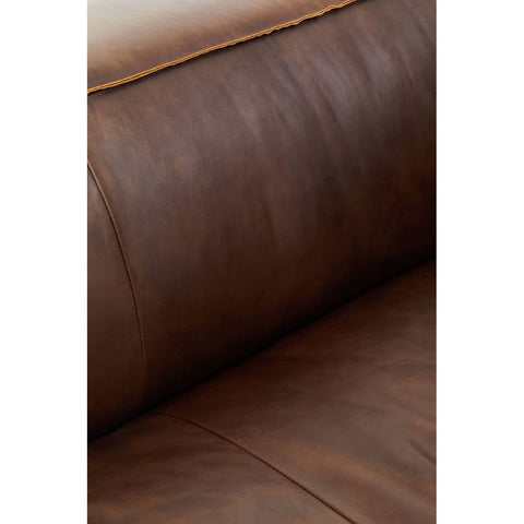 Close-up view of the antique brown leather upholstery of a two-seater sofa, showcasing the rich texture and subtle creases of the leather. The warm tones highlight the sofa's vintage appeal, with a smooth surface and a hint of sheen