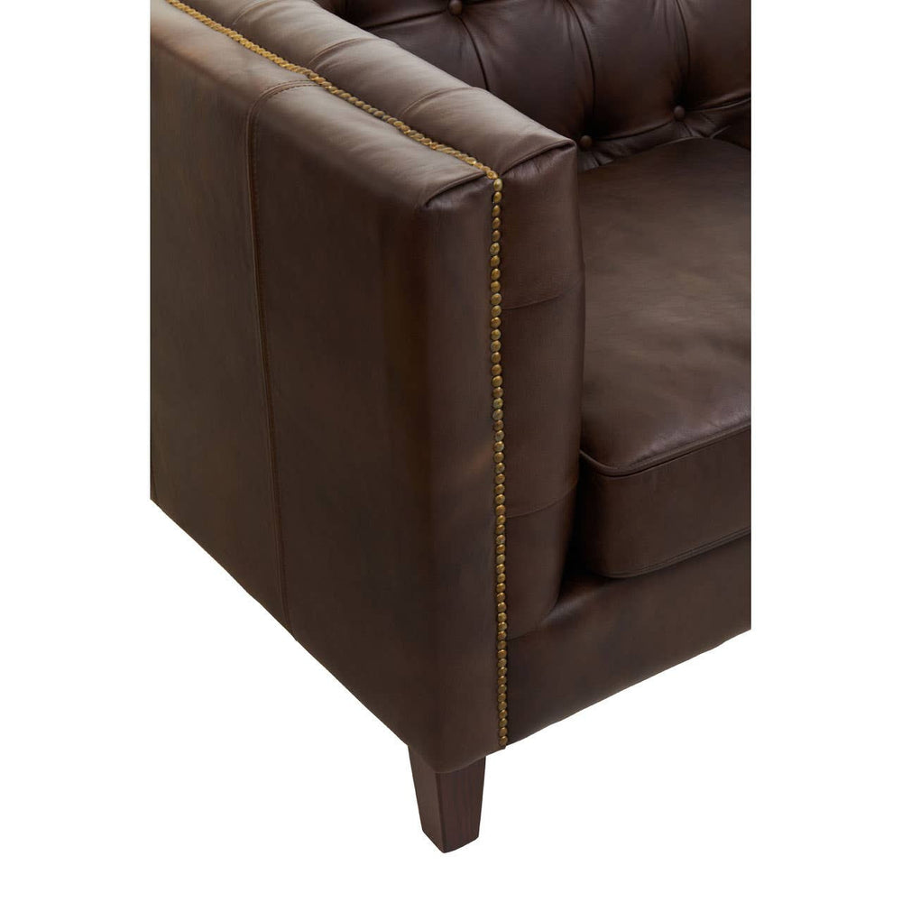 Dark brown leather corner of a modern Chesterfield sofa, featuring a tufted design and a sturdy wooden leg. The upholstery has a smooth finish, highlighting the rich color and texture of the leather