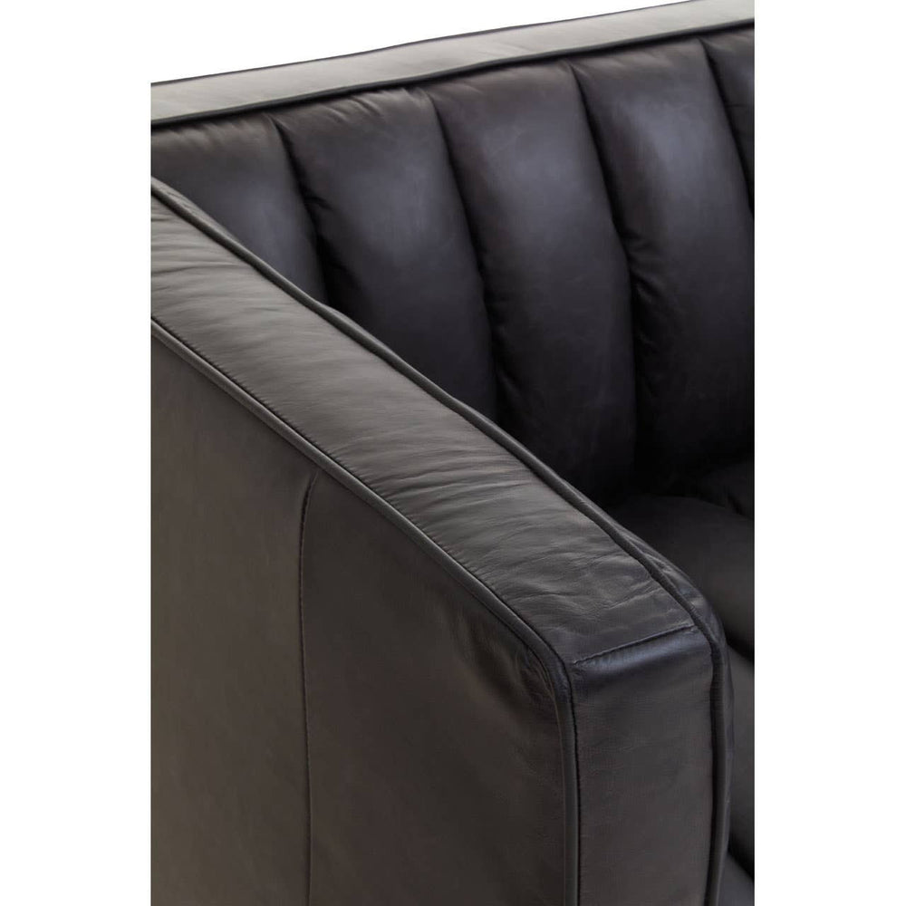 Close-up view of the flared armrest of a black leather sofa, showcasing its smooth texture and tufted design. The leather appears soft and well-crafted, highlighting the modern aesthetic of the furniture piece
