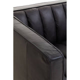 Close-up view of the flared armrest of a black leather sofa, showcasing its smooth texture and tufted design. The leather appears soft and well-crafted, highlighting the modern aesthetic of the furniture piece