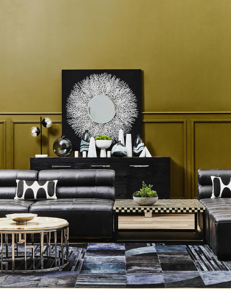 Antique black leather modular sofa chair with a sleek, armless design, positioned in a stylish living space featuring a gold wall, decorative artwork, and modern furniture elements