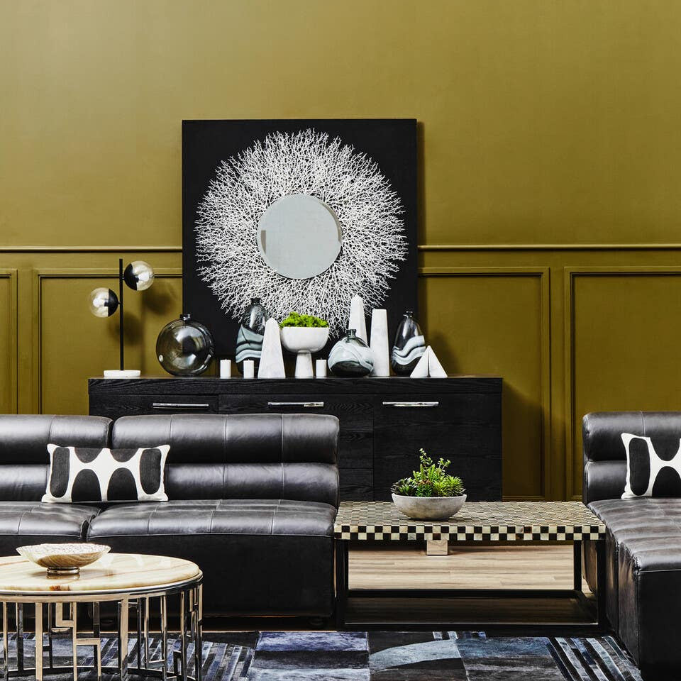 Antique black leather modular sofa chair with a sleek, armless design, positioned in a stylish living space featuring a gold wall, decorative artwork, and modern furniture elements