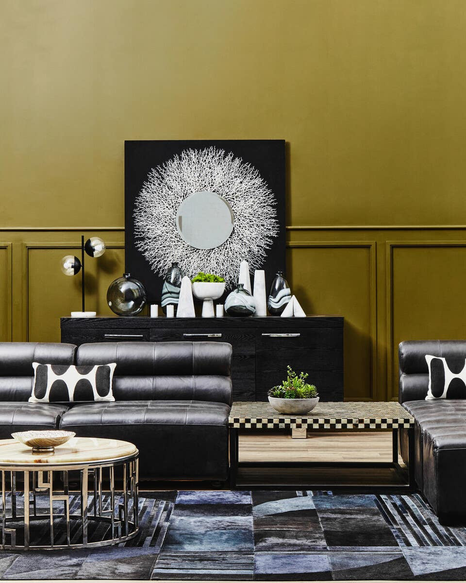 Antique black leather modular sofa chair with a sleek, armless design, positioned in a stylish living space featuring a gold wall, decorative artwork, and modern furniture elements