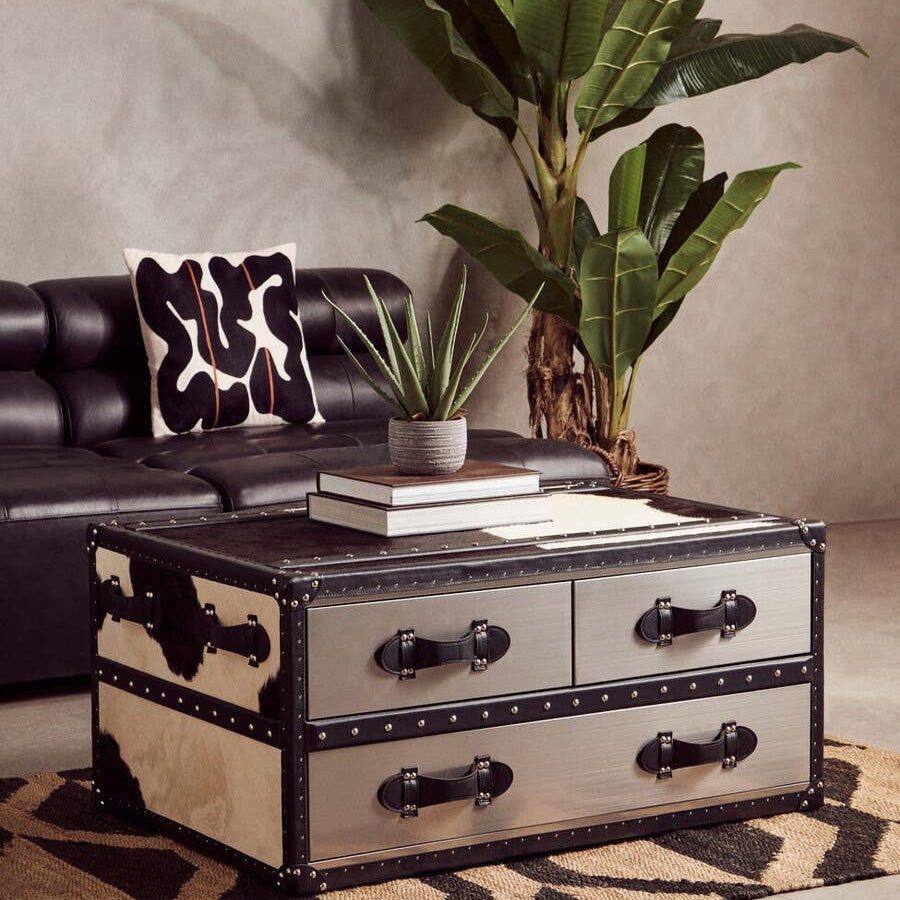Antique black leather modular sofa chair with a sleek armless design, placed next to a stylish coffee table featuring two drawers, set on a patterned rug. A large green plant adds a touch of nature to the modern living space