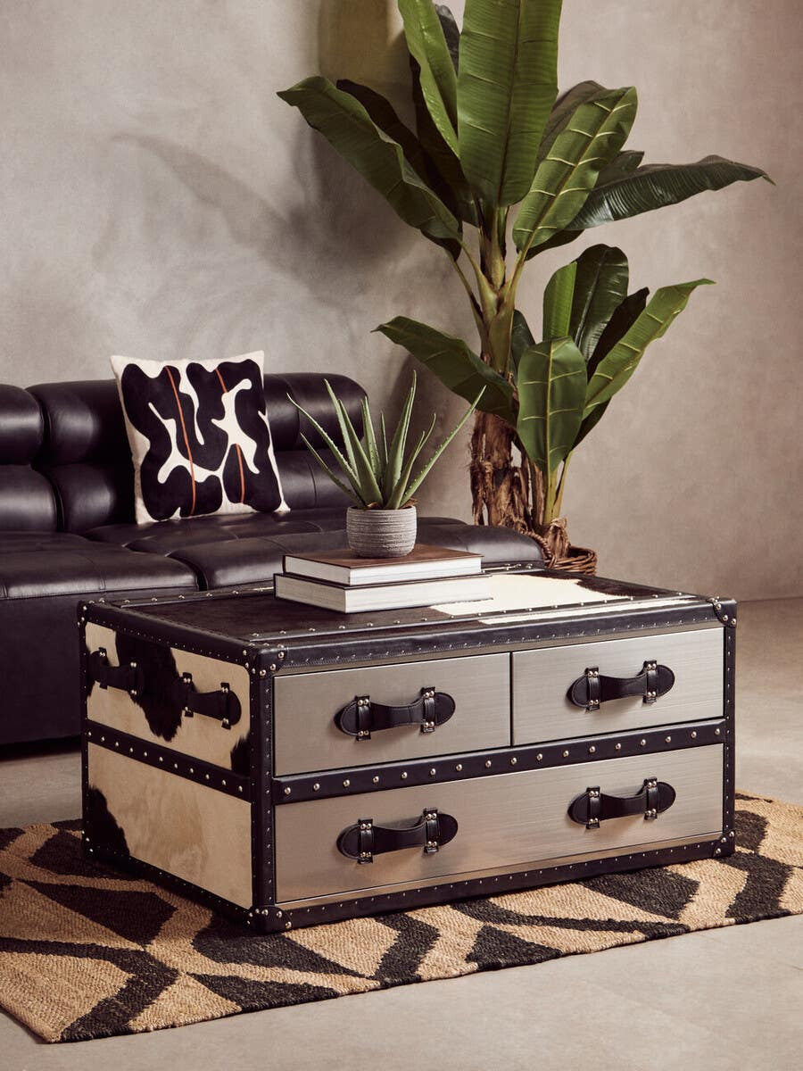 Antique black leather modular sofa chair with a sleek armless design, placed next to a stylish coffee table featuring two drawers, set on a patterned rug. A large green plant adds a touch of nature to the modern living space